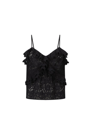 A woman modeling a black lace camisole top with ruffle trim and matching black lace pants against a warm beige textured wall.