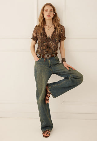 A woman modeling a brown patterned short-sleeve blouse and wide-leg blue jeans with brown sandals