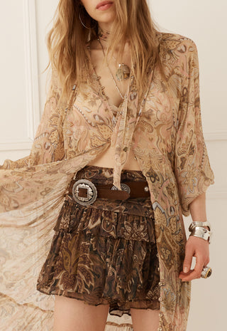 A woman wearing a bohemian-style outfit featuring a sheer beige paisley cardigan