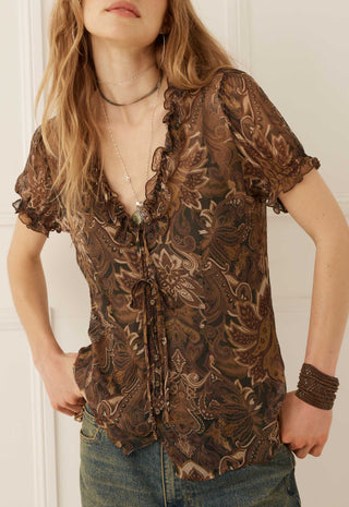 A woman wearing a brown and beige paisley patterned sheer blouse with ruffle trim