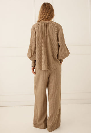  paired with brown strappy flat sandals against a white paneled wall.