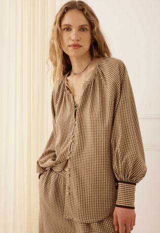 A woman wearing a brown and beige gingham long-sleeve blouse with a gathered neckline and balloon sleeves