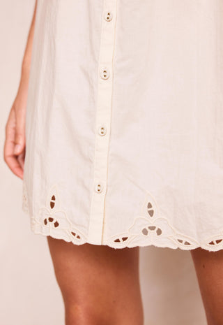 Close-up of a cream-colored eyelet button-down dress with a scalloped hem, worn by a model.