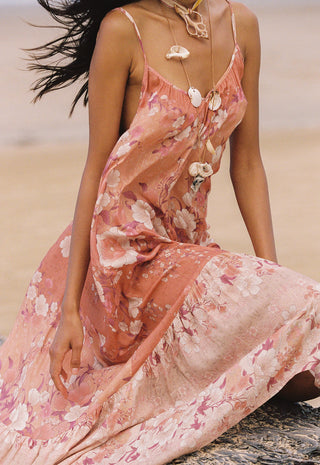  posed outdoors against a clear blue sky with a palm tree visible behind her.