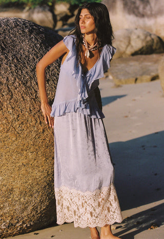 A woman stands outdoors on a sandy beach next to a large rock